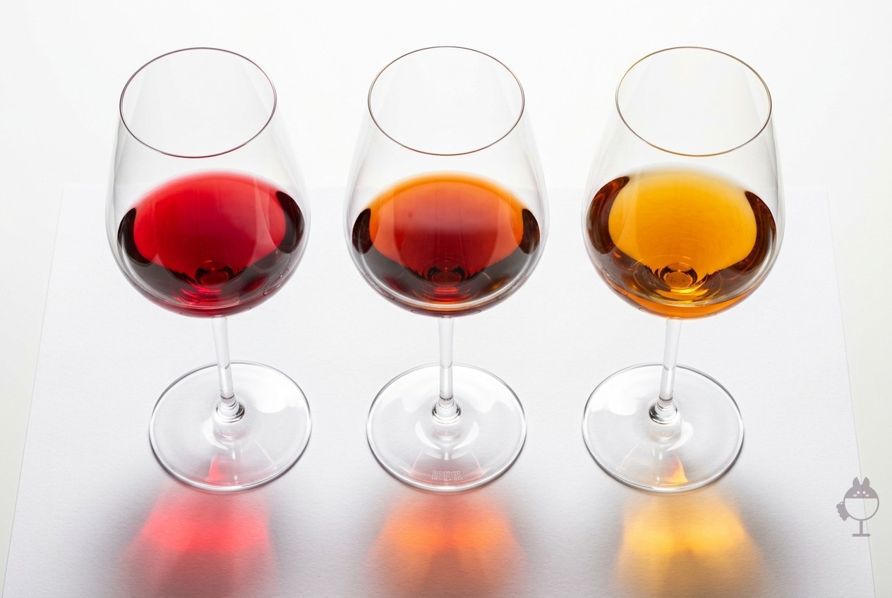 Trois verres à vin sur papier blanc vus d'en haut, contenant un vin rouge, un vin tuilé et un vin ambré